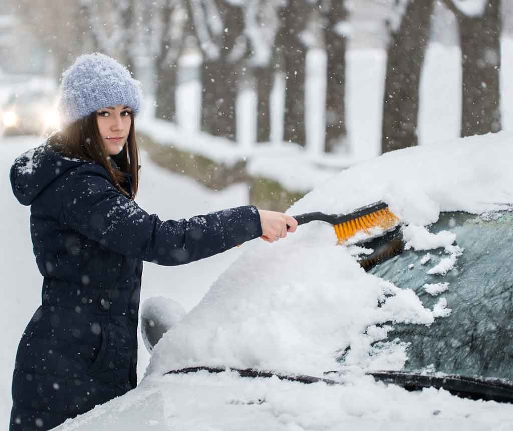 凍った車のフロントガラスを取り除く女性