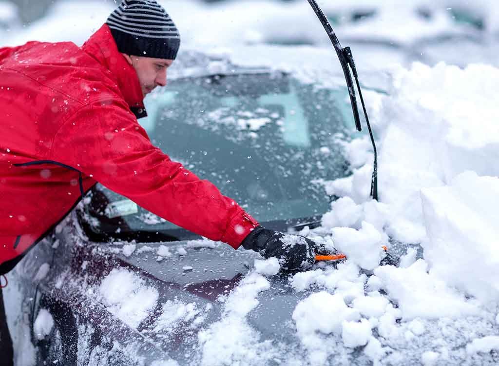 車に積もった雪かきをする男性
