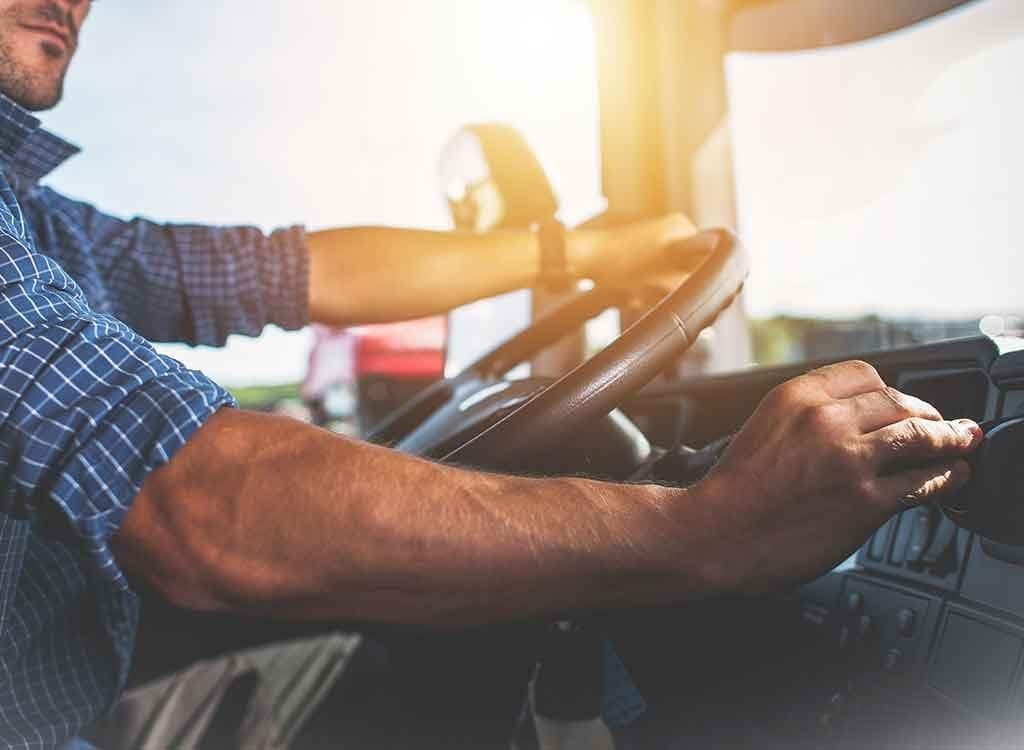 腕まくりでハンドルを握るトラックドライバー